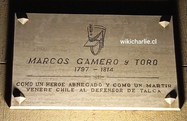 La imagen nos muestra la placa eregida al héroe TALQUINOS Marcos Gamero de 19 años, quien defendió la bandera chilena, en la Plaza de Armas de Talca. Está se encuentra a un costado del edificio del Banco Talca, en 1 sur con 1 oriente.