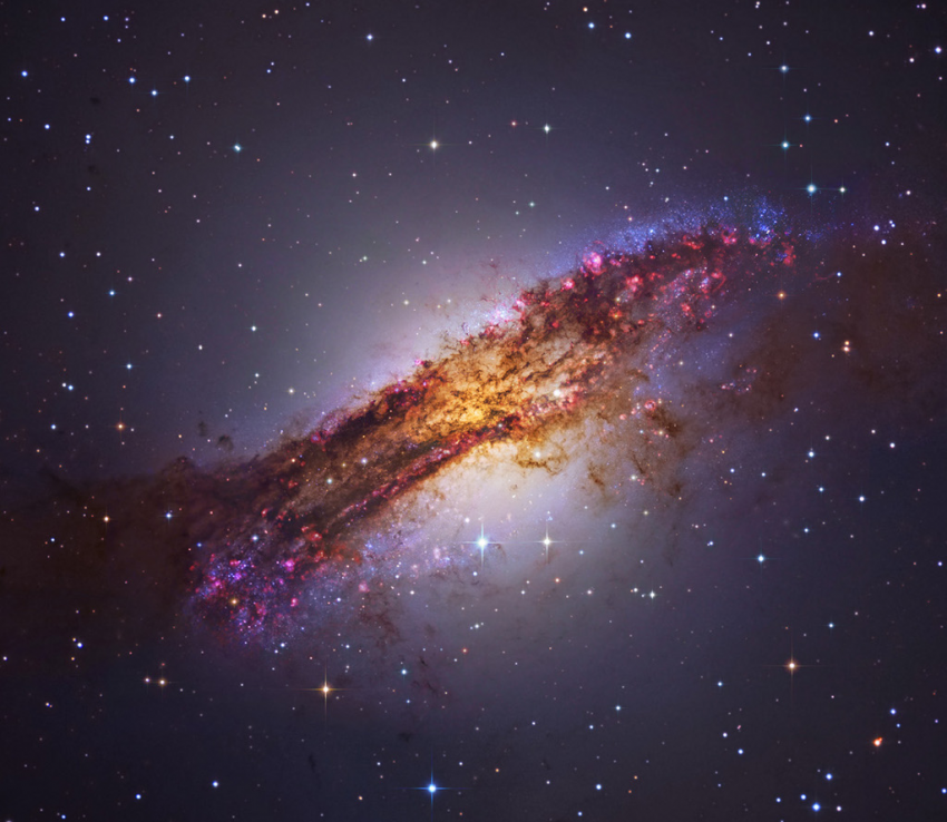 la galaxia activa más cercana al planeta Tierra? Pues Centaurus A, que está a tan sólo 11 millones de años luz. Esta peculiar galaxia elíptica, que abarca más de 60.000 años luz, también se conoce como NGC 5128. Forjada en una colisión de dos galaxias normales, Centaurus A es un fantástico revoltijo de cúmulos de estrellas azules, regiones rosadas de formación estelar e imponentes bandas de polvo oscuro que aquí se ven con un detalle considerable. La fotografía es una combinación de datos de telescopios espaciales y terrestres, grandes y pequeños. Cerca del centro de la galaxia, los restos cósmicos son consumidos ininterrumpidamente por un agujero negro central con una masa mil millones de veces la del Sol. Como en otras galaxias activas, este proceso genera energía de rayos gamma, rayos X y radio emitida por Centaurus A.