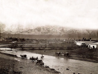 Carretelas y Carruajes a orillas del río Mapocho en Santiago, 1875. La imagen es frente al Puente de Carros (actual Puente del Obelisco frente al Mercado Tirso de Molina), y el de mas atrás es el Puente de Palos. Véase: Carretas Chilenas